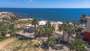 A coastal residential area with modern buildings, palm trees, and a view of the sea. - Villa Alegria (Cabo San Lucas)