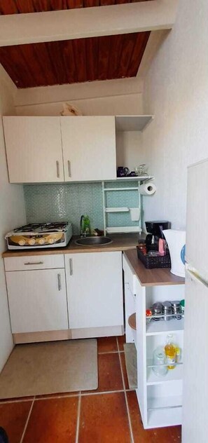 Compact kitchen with gas stove, sink, and refrigerator, featuring white cabinetry and a tiled floor.