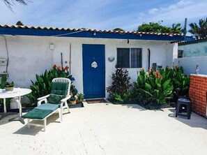 Relax on the patio with a table and chair, surrounded by lush greenery and a charming entrance.