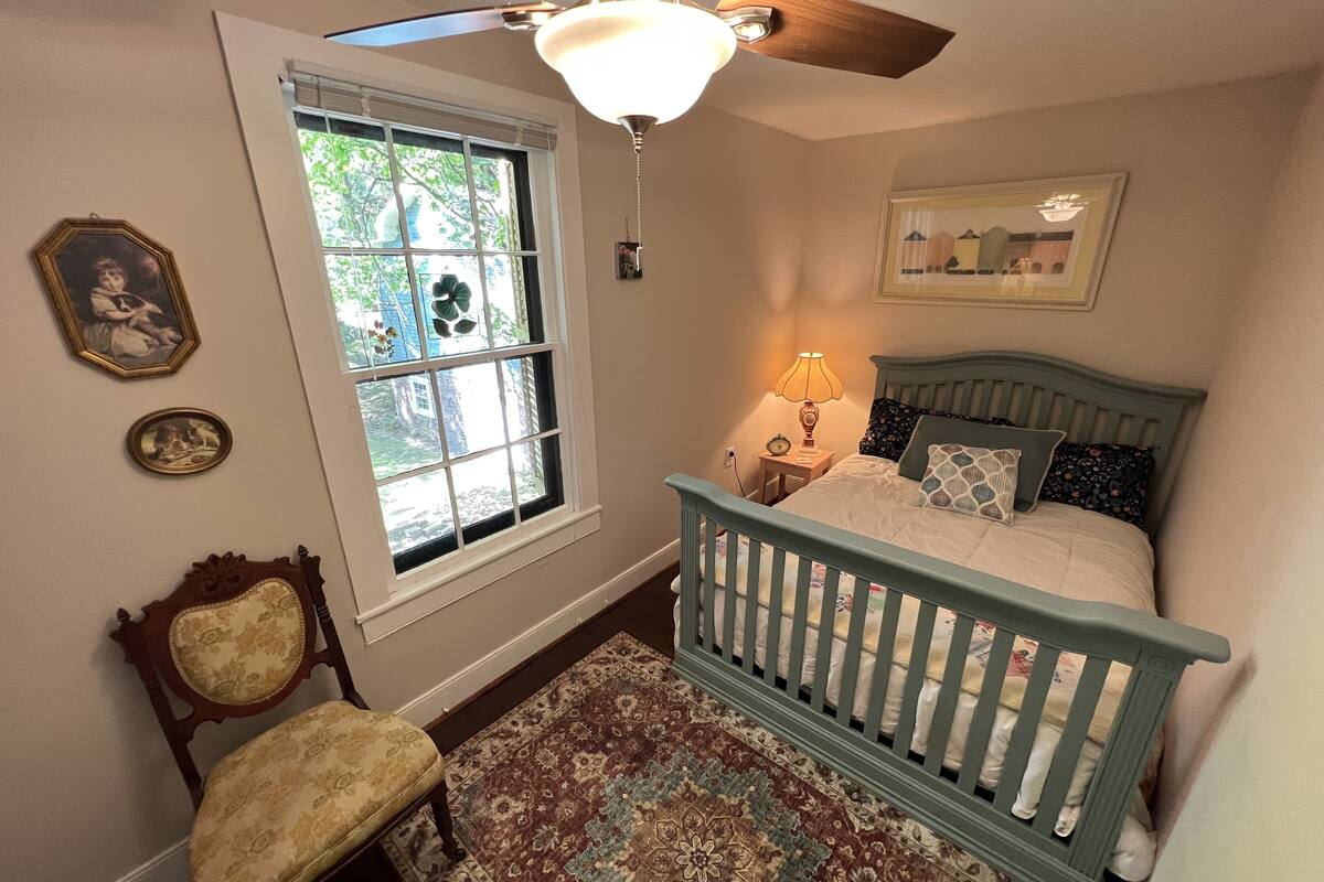 A bedroom with a wooden bed, a chair, a window with a view, a ceiling fan, and a bedside lamp.