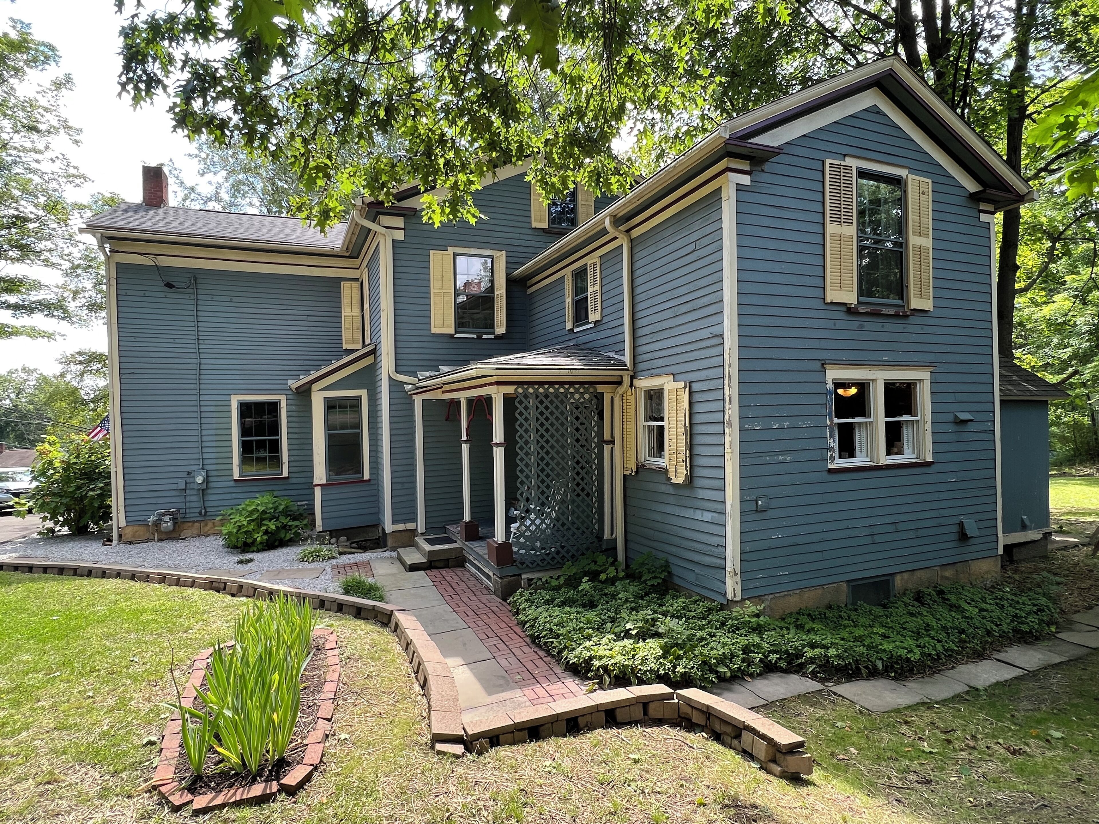 A two-story house with a porch and a brick pathway leading to the entrance.