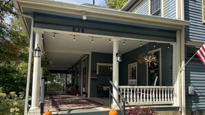 A porch with a white railing, a wooden bench, and a small table. - Highland Guesthouse (Meadville)