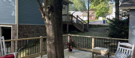 A wooden deck with a large tree, a stone wall, and a staircase leading to a second-story balcony.