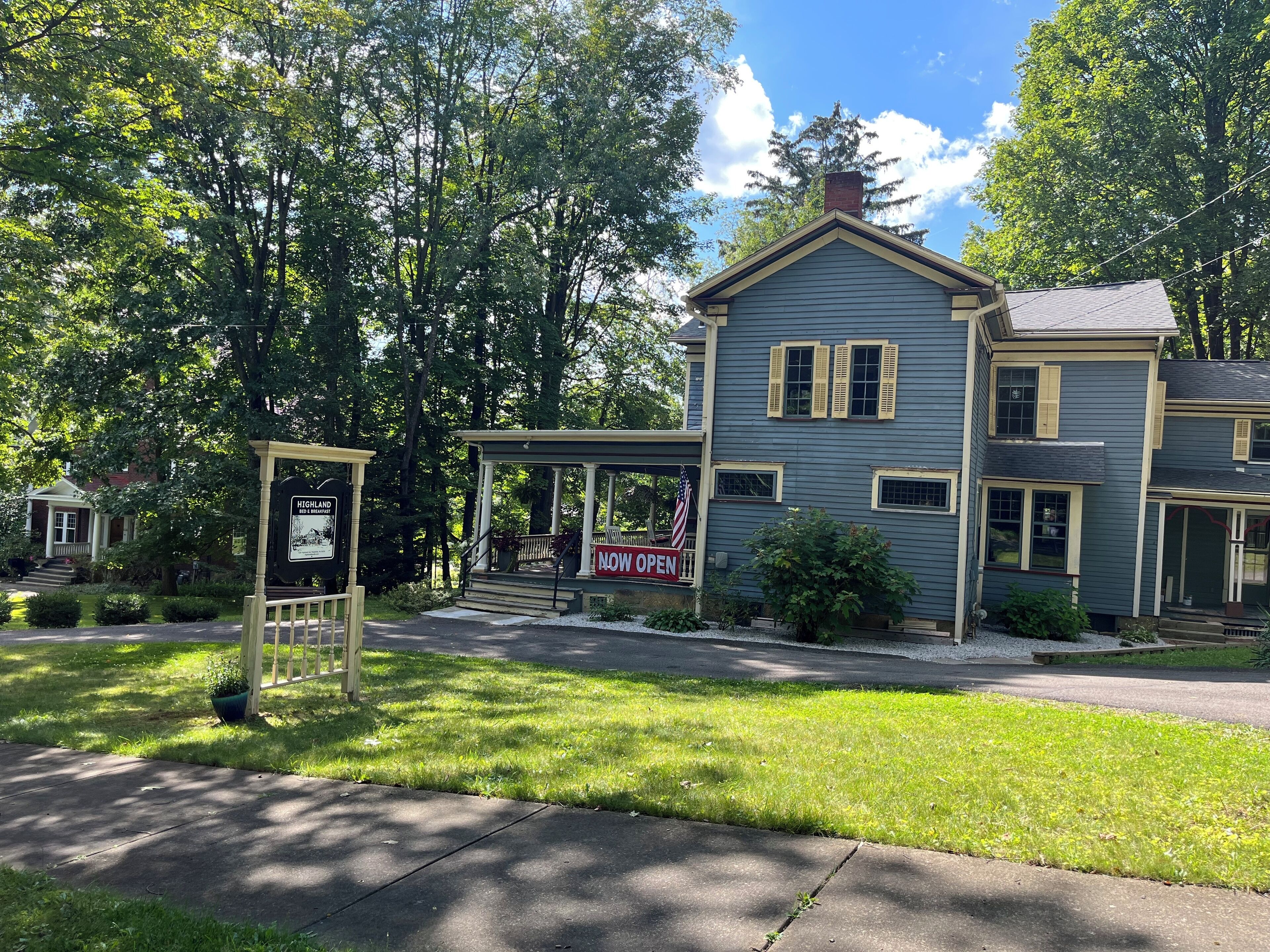 A two-story house with a porch, a sign indicating it is now open, and a small garden area.