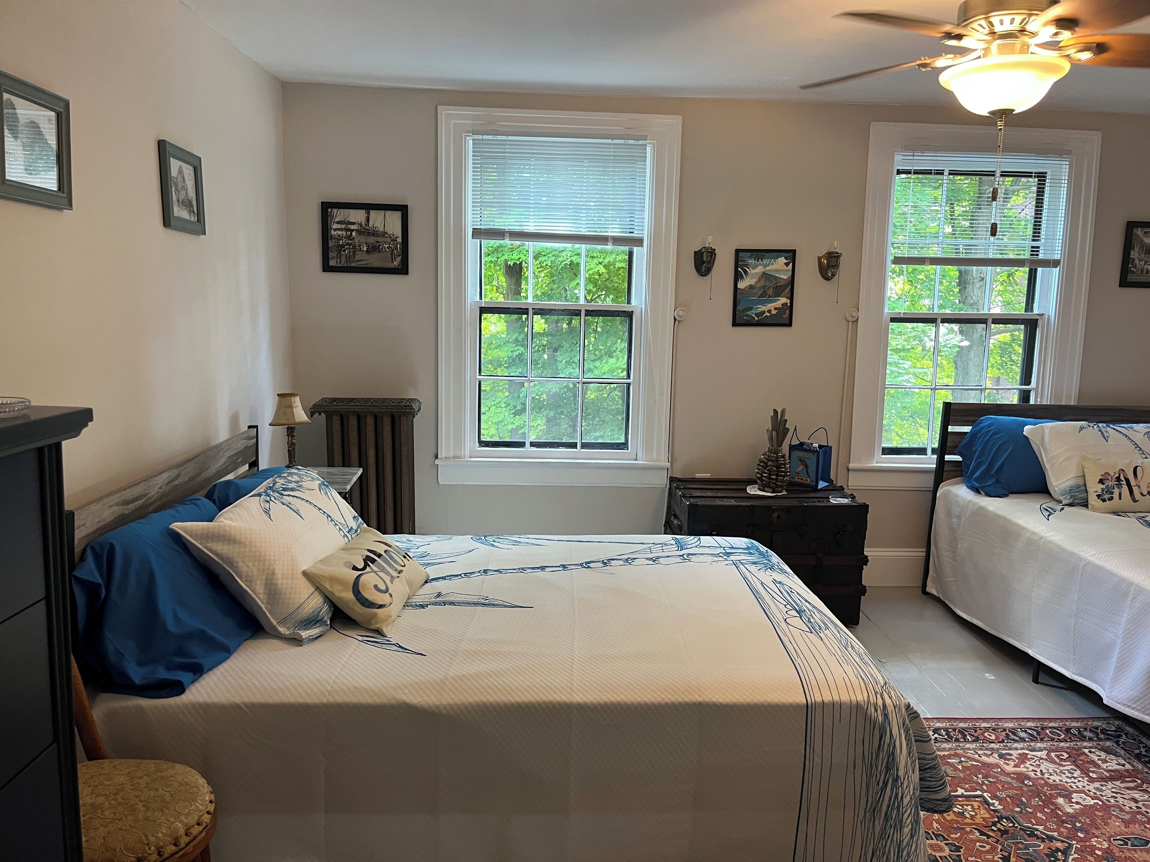 A bedroom with two beds, a ceiling fan, and a window with a view of trees.