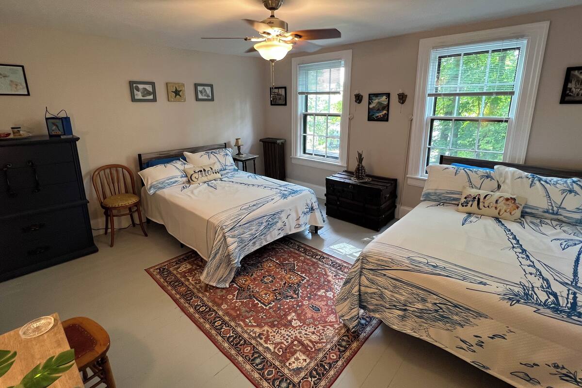 A bedroom with two beds, a ceiling fan, and a large window.