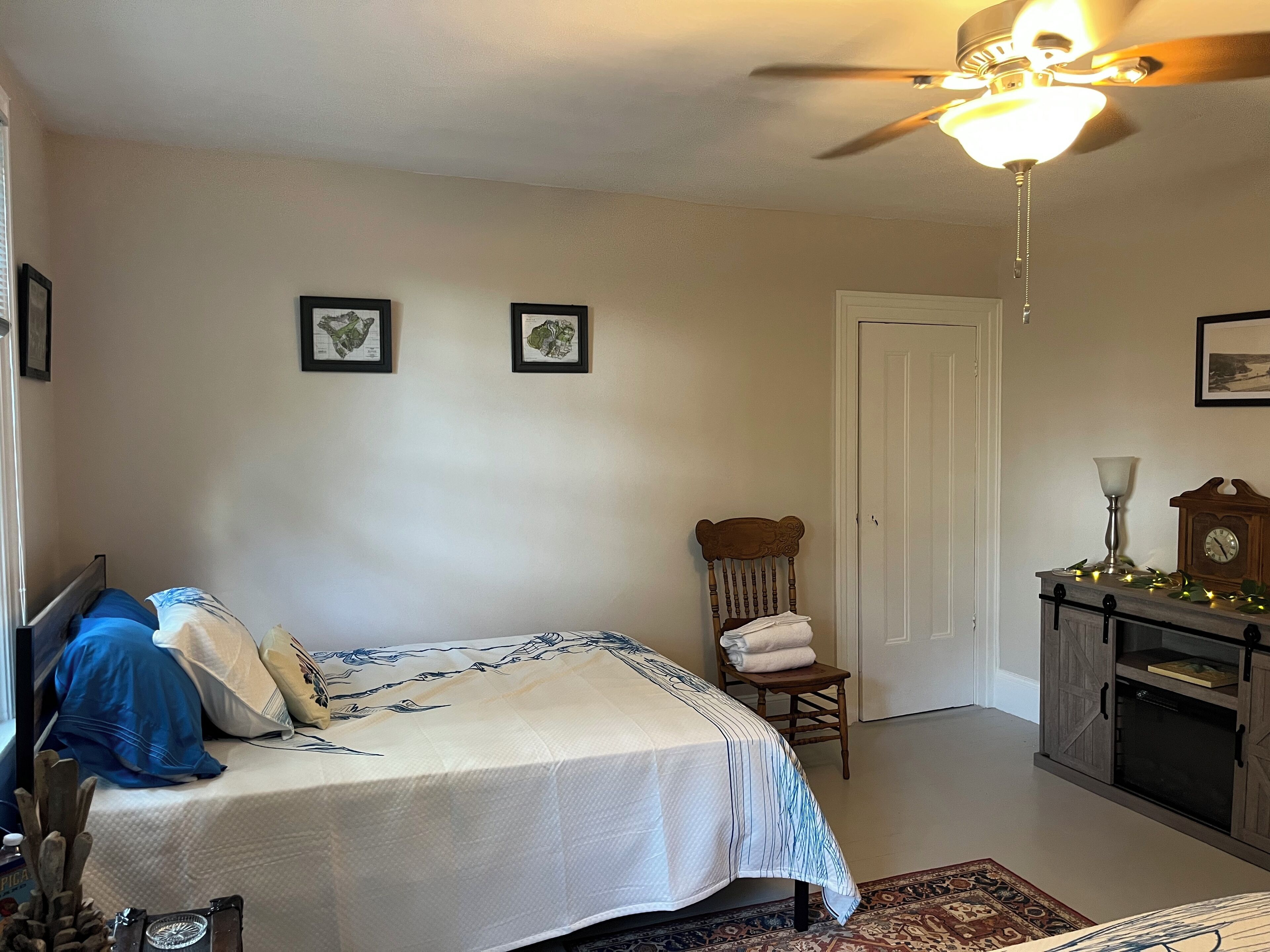 A bedroom with a bed, a chair, a desk with a lamp, and a ceiling fan.