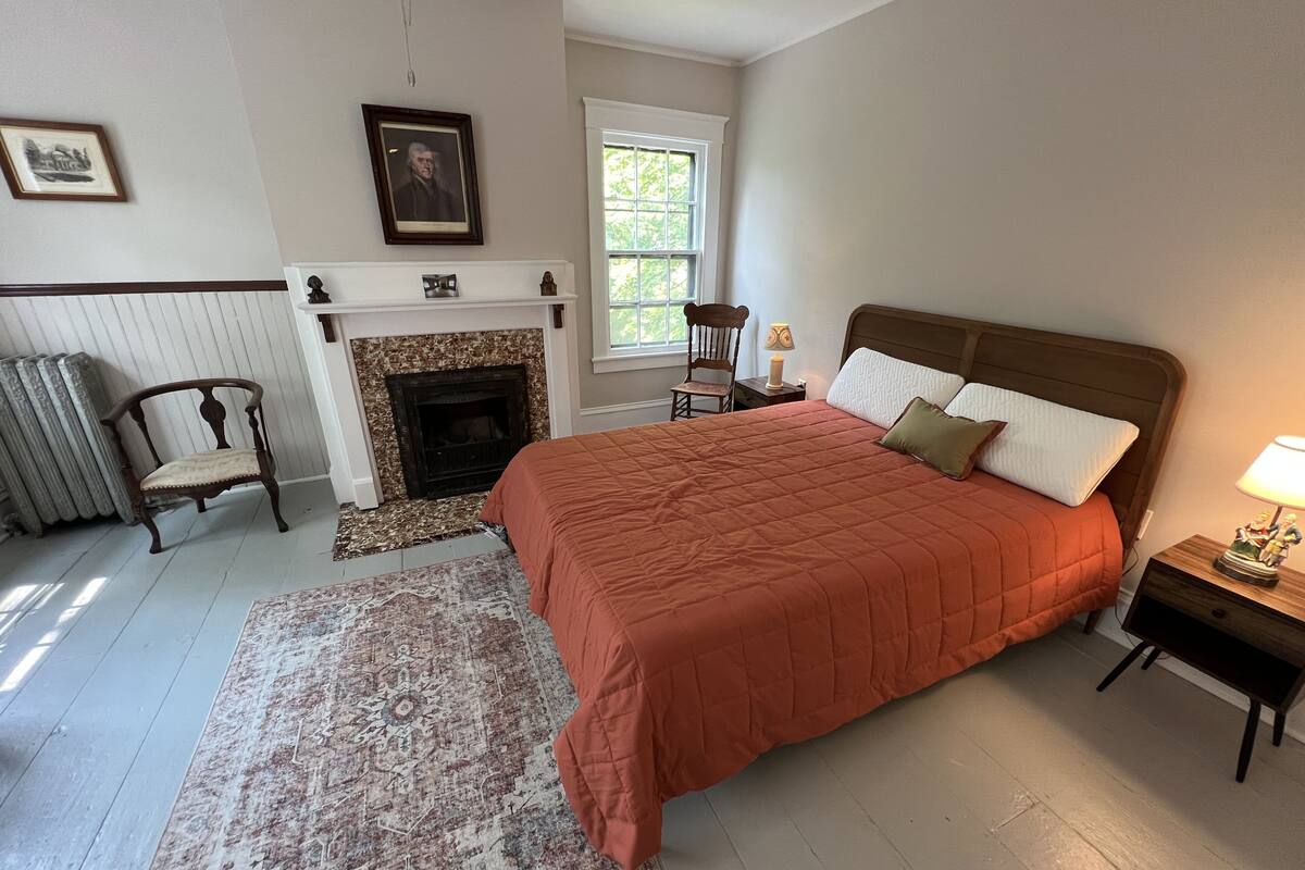A bedroom with a large bed, a fireplace, a chair, and a window.