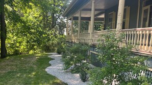 A covered porch with columns, a gravel path, and surrounding greenery. - Highland Guesthouse (Meadville)