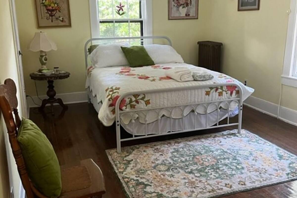 A bedroom with a bed, a chair, a window, a ceiling fan, and a rug.
