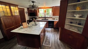 A kitchen with wooden cabinets, a marble countertop, a central island, and a built-in shelf with decorative items. - Highland Guesthouse (Meadville)