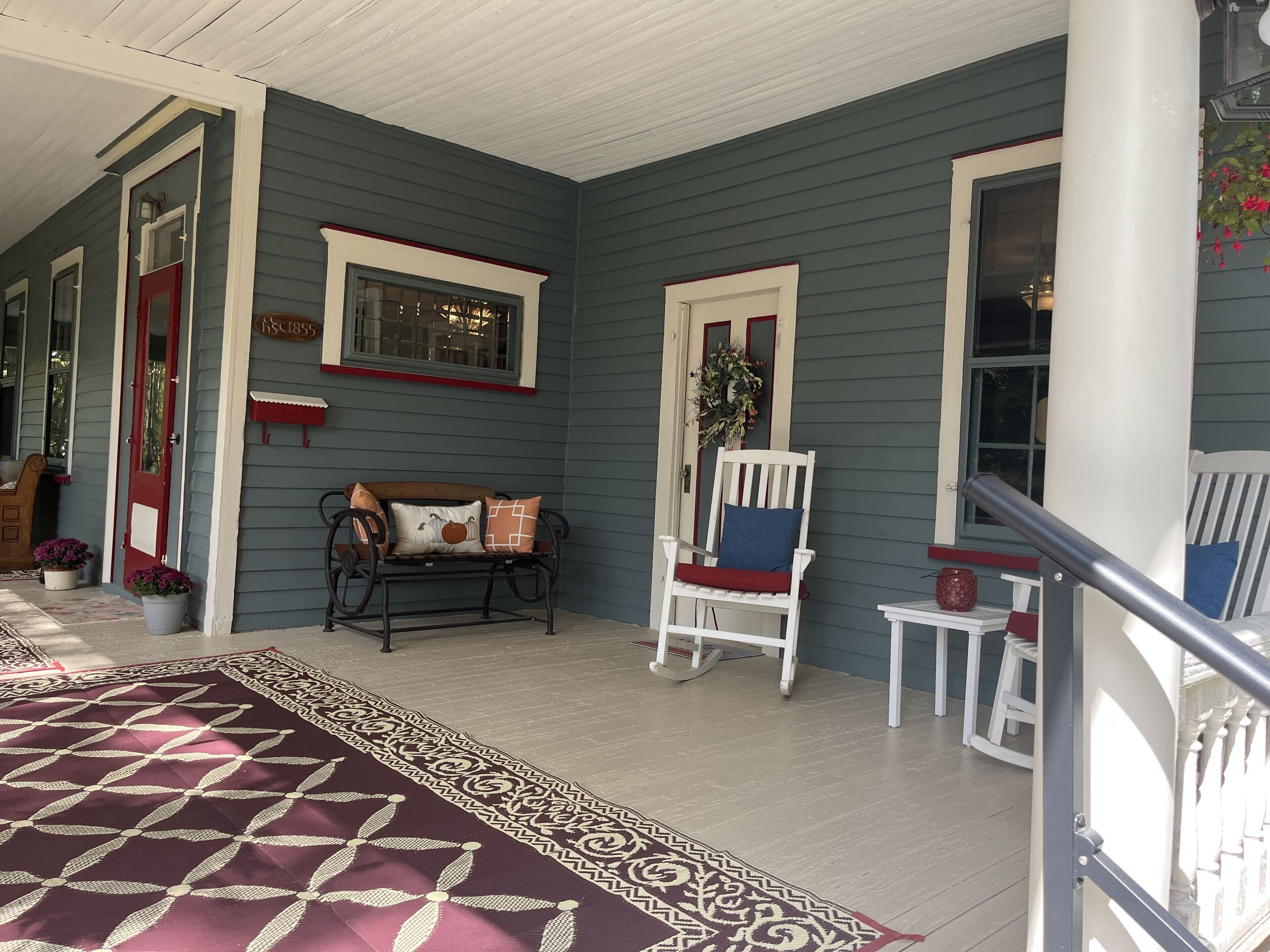 A porch with a patterned rug, a bench, and a white chair.
