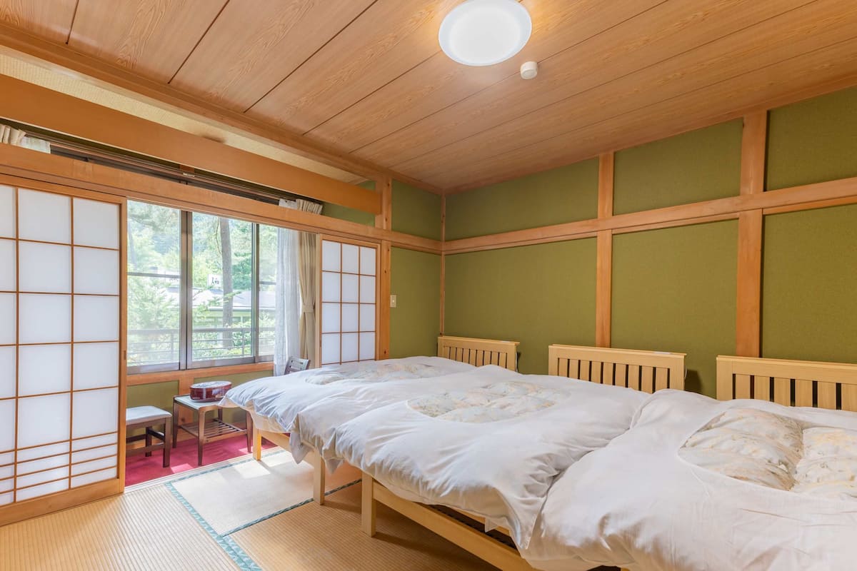 Ett traditionellt japanskt rum med tatamimattor på golvet, en futonmadrass, en shojiskärm och utsikt över grönskan utanför.