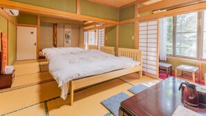Una habitación tradicional japonesa con suelo de tatami, una cama de madera, una mesita con hervidor y puertas correderas.