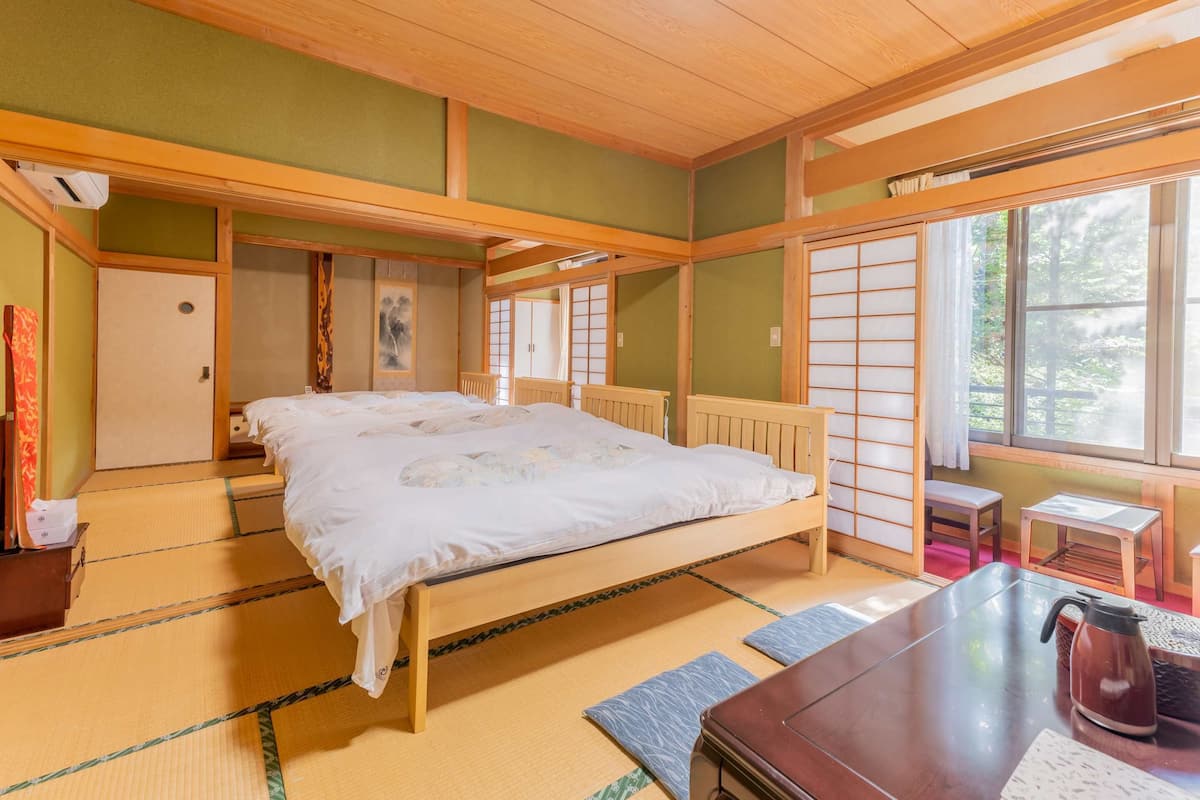 Ett traditionellt japanskt rum med tatamimattor på golvet, en säng av trä, ett litet bord med en vattenkokare och skjutdörrar.