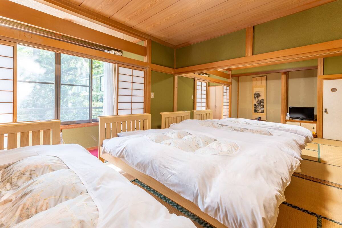 Ett traditionellt japanskt rum med tatamimattor på golvet, en stor säng med vita sängkläder, en tv och skjutdörrar.