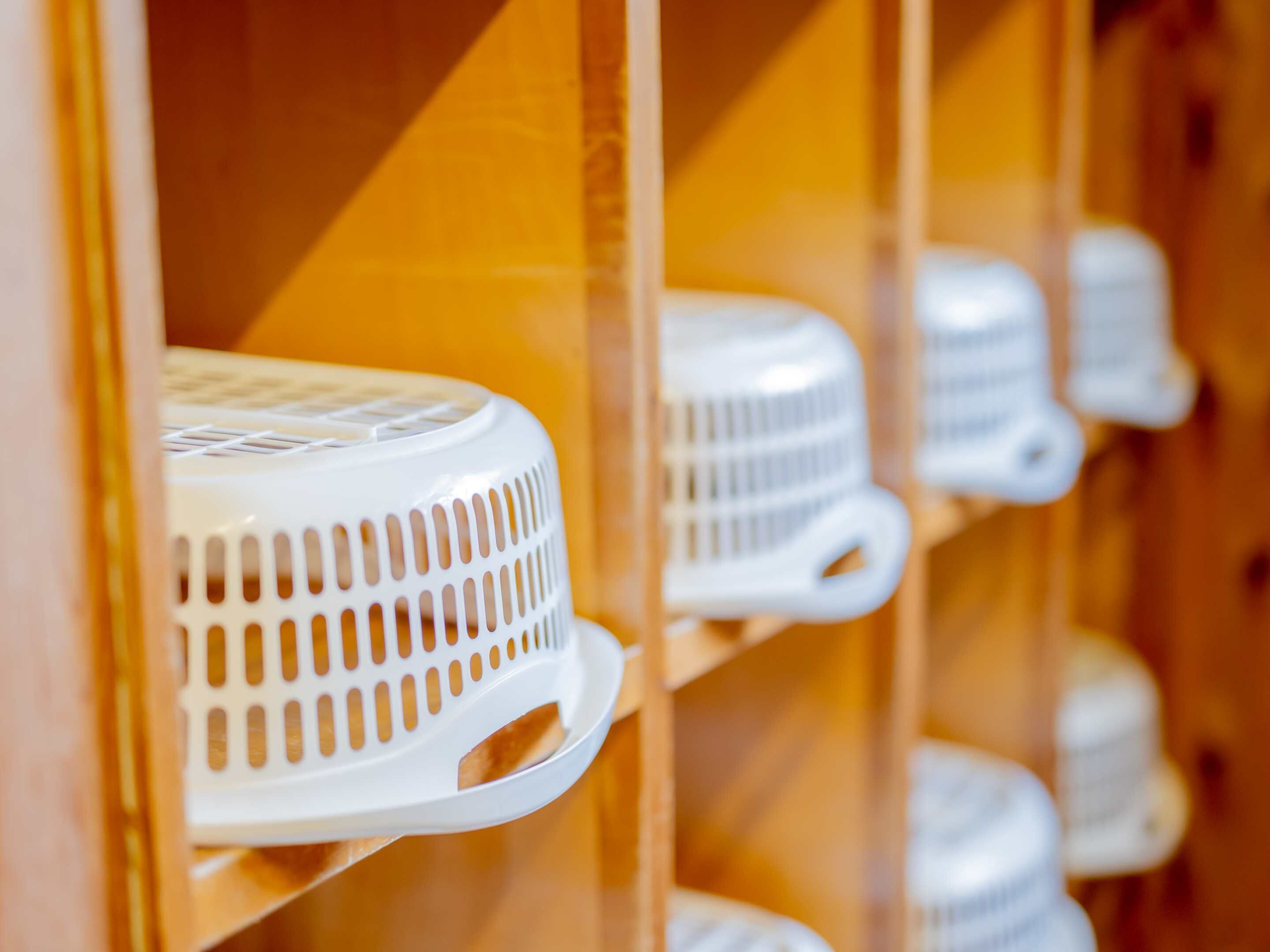 A row of white, round, white ceramic plates with handles, arranged on wooden shelves.