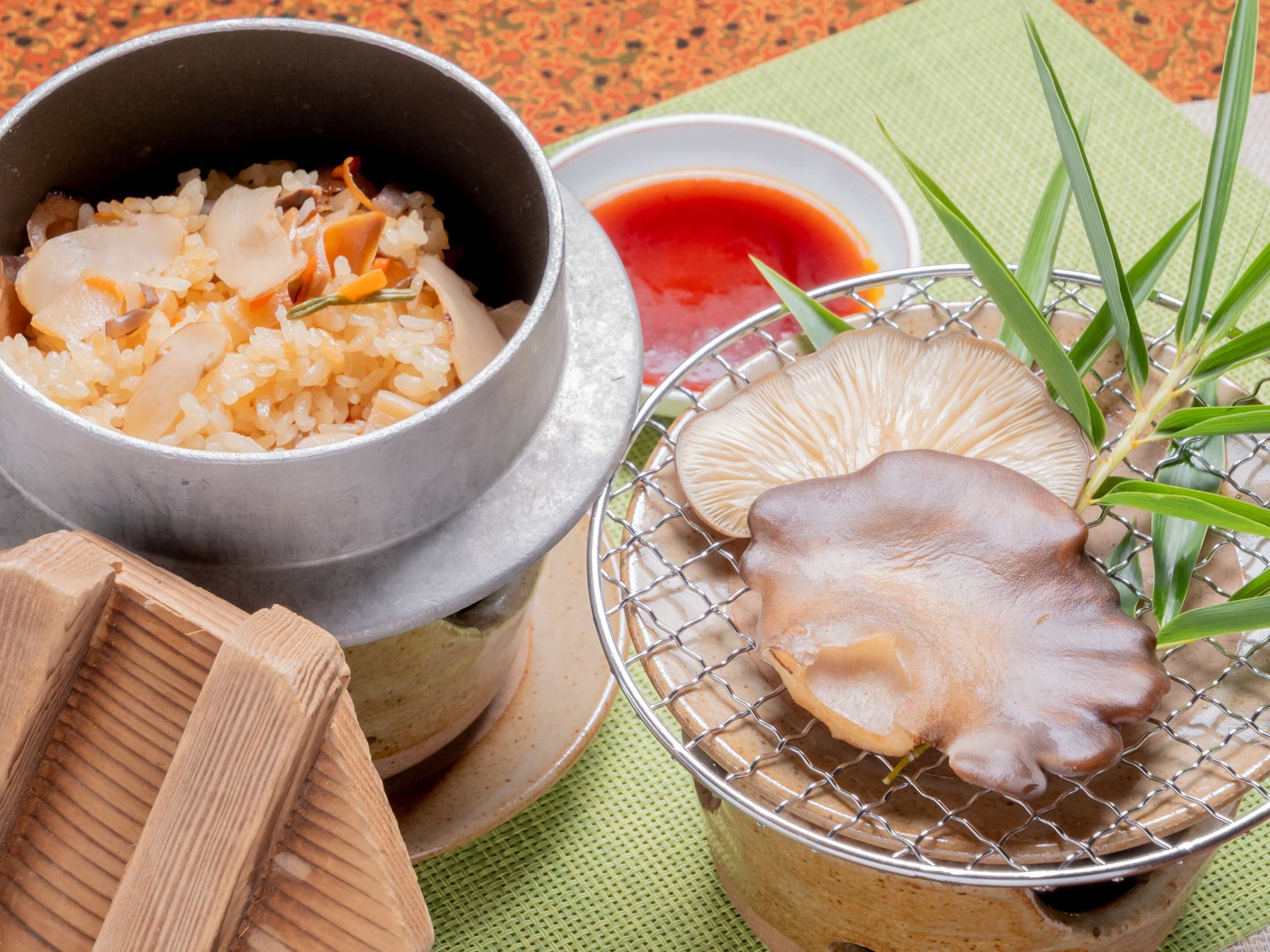 A bowl of rice with vegetables, a small bowl of sauce, and a mushroom on a wire rack.
