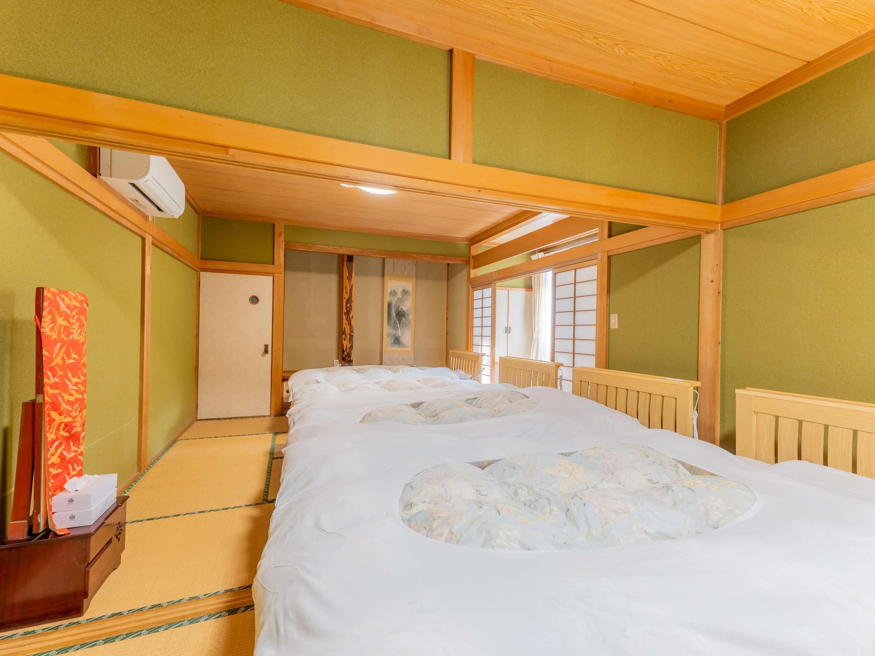 Una habitación tradicional japonesa con suelo de tatami, una cama grande con futón, una puerta corrediza de shoji y un baúl para guardar futones.