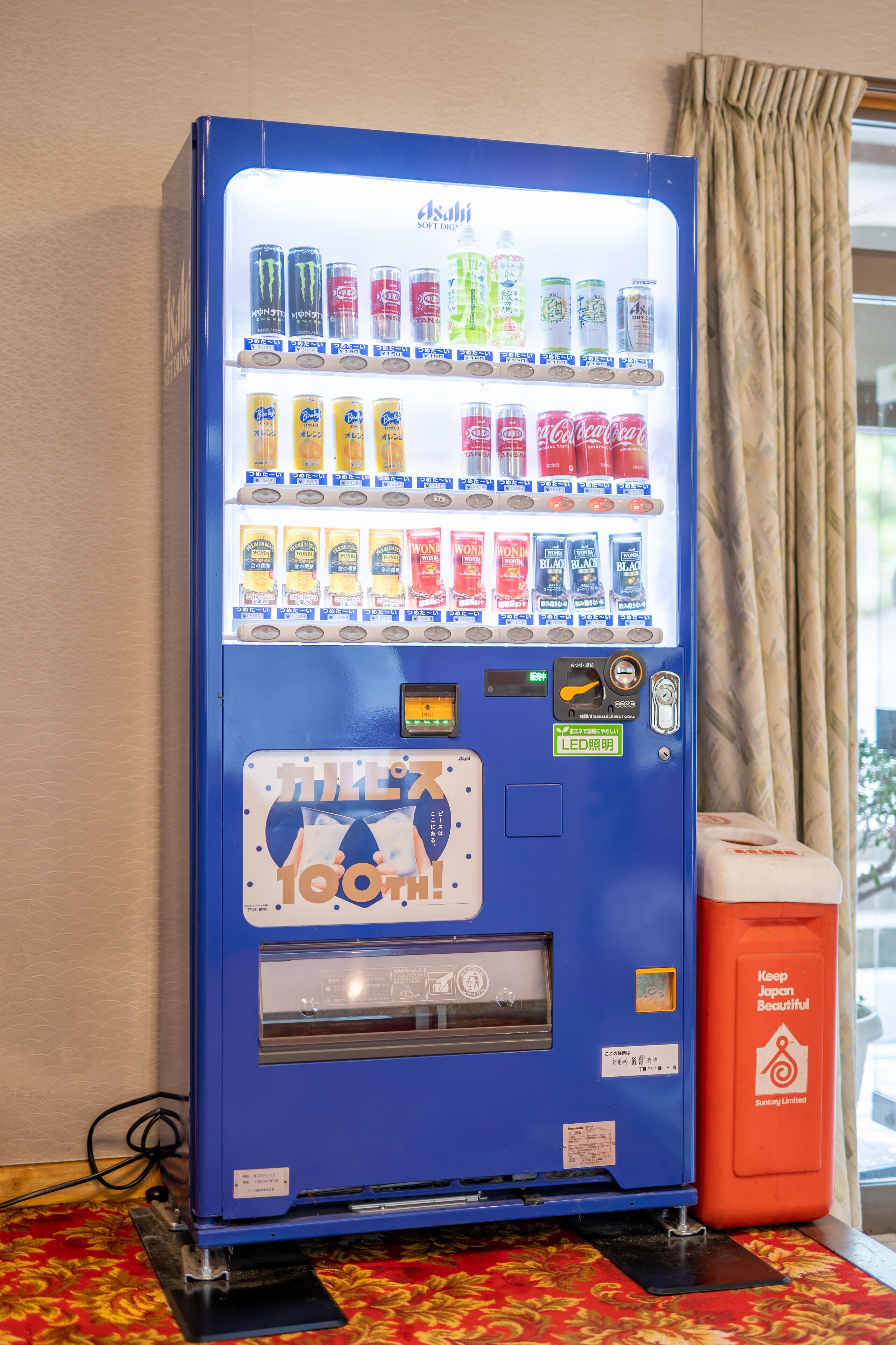 A vending machine with various drinks and snacks, a payment slot, and a recycling bin.
