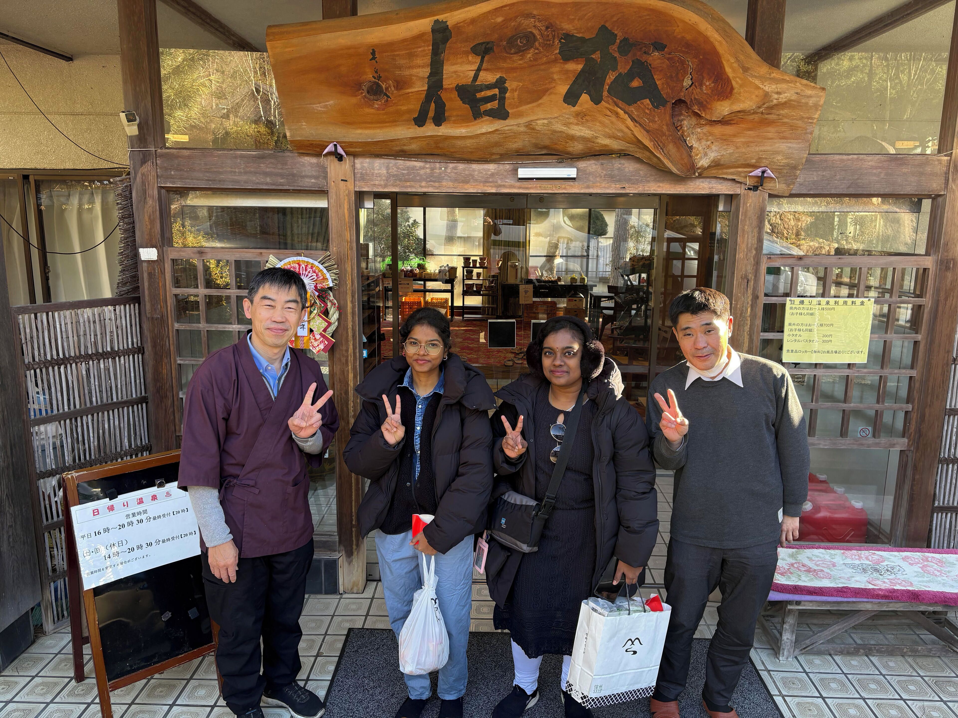 A wooden sign with characters, a glass door entrance, a mat, and a table with a floral tablecloth.