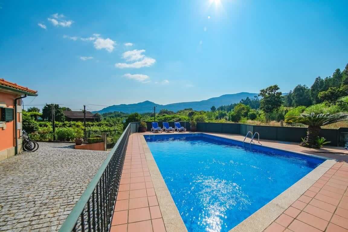 A swimming pool with a tiled deck, a bicycle, and a view of hills in the background.