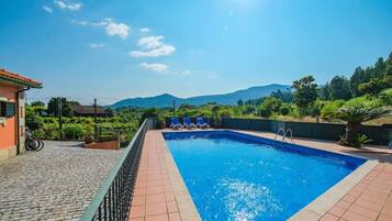 A swimming pool with a tiled deck, a bicycle, and a view of hills in the background.