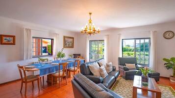 A living room with a sofa, dining table, chairs, and a chandelier.