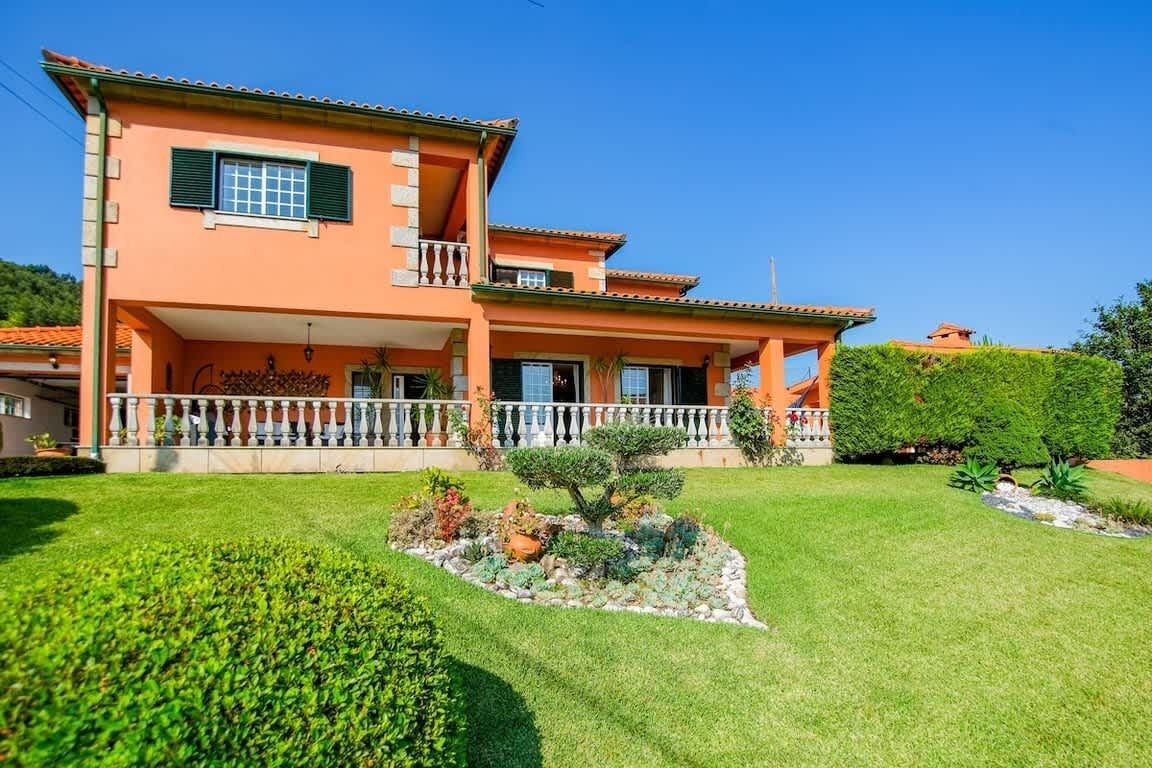 Una casa de dos plantas con balcón, césped cuidado y un pequeño jardín.