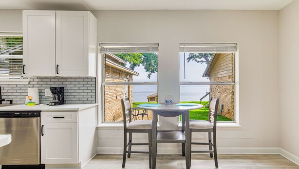 A kitchen with white cabinets, a dishwasher, and a window overlooking a backyard. - Gulf Breeze Bayfront Bungalow - Dock - Pet-Friendly - Near Pensacola Beach (Gulf Breeze)