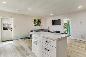 A modern kitchen with white cabinetry, a large island, and a flat-screen TV mounted on the wall.