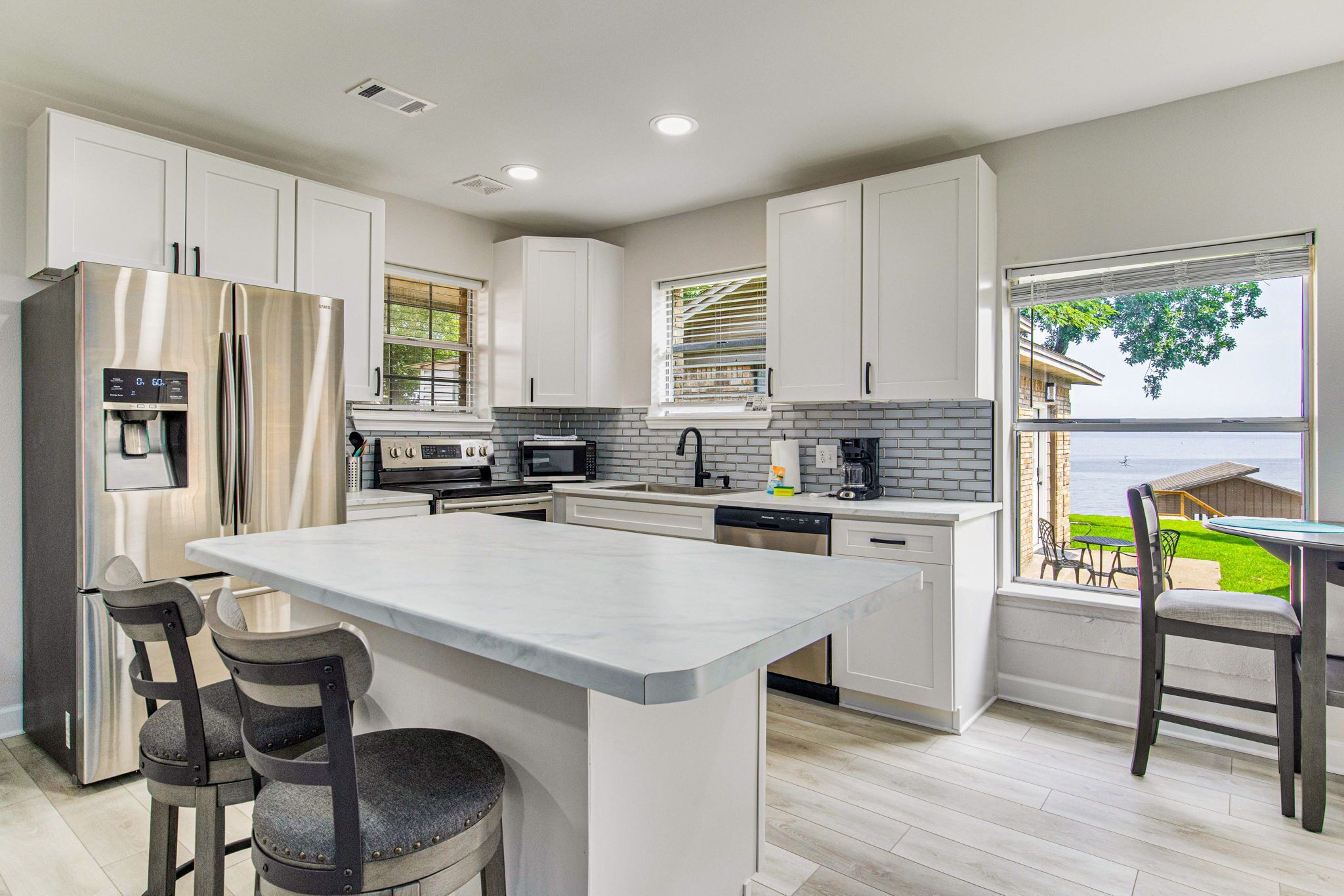 A modern kitchen with white cabinets, stainless steel appliances, and a large island.