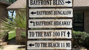 Wegwijzer met pijlen naar Bayfront Bliss, Bayfront Bungalow, Bayfront Hideaway, met afstanden naar de baai en het strand.