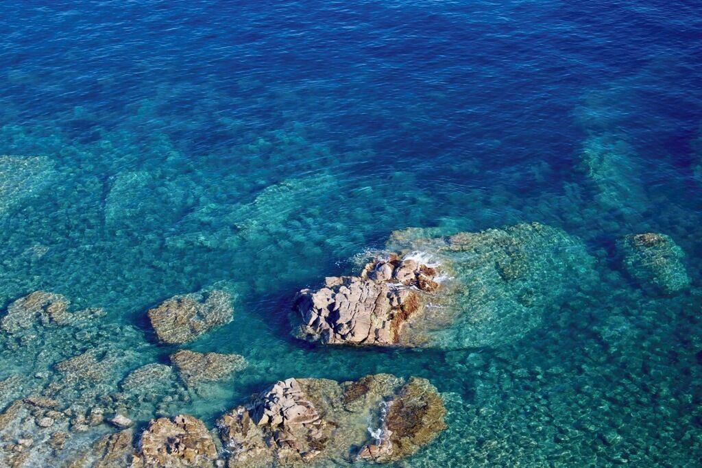 An aerial view of a coastal area with clear blue water and rocky formations.