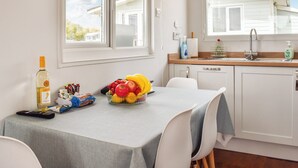 A kitchen with a dining table set for two, a fruit bowl, a bottle of wine, and a remote control. - 2 bedroom accommodation in Hayle (Hayle)