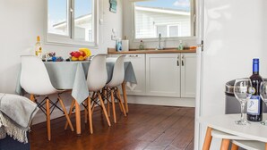 A dining area with a table set for four, a kitchen with white cabinets, and a wine bottle on the counter. - 2 bedroom accommodation in Hayle (Hayle)