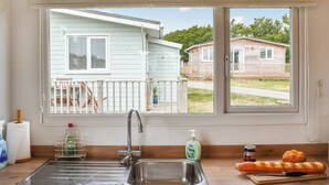 A kitchen with a stainless steel sink, a window with a view of two mobile homes, a bottle of dish soap, and a loaf of bread on the counter. - 2 bedroom accommodation in Hayle (Hayle)