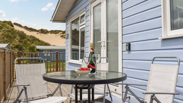 A glass table with a bowl of strawberries and a bottle of champagne on a deck with white chairs. - 2 bedroom accommodation in Hayle (Hayle)