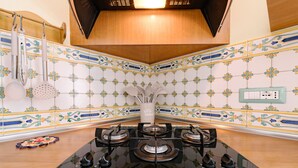 A kitchen with a four-burner gas stove, a hanging rack with kitchen utensils, and a decorative backsplash.