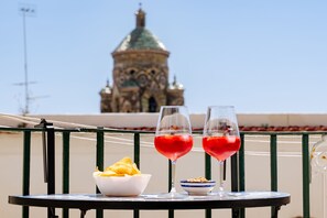 A table with two glasses of red drink, a bowl of chips, and a small dish of nuts on a balcony with a view of a historic building. - Amalpha Domus Apartment (Amalfi)