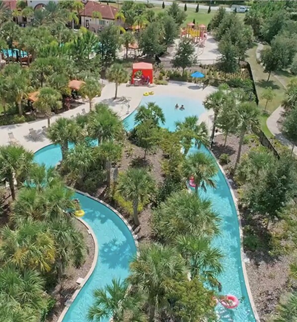 Relax by the resort's winding pool surrounded by lush greenery and palm trees, with lounge chairs and umbrellas at your disposal.