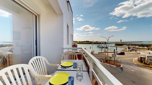 A balcony with a table set for two, overlooking a harbor with boats and a lighthouse.