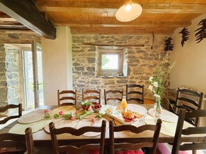 Ein rustikaler Essbereich mit Steinwand, Holzbalken an der Decke und einem Tisch, der zum Essen gedeckt ist.