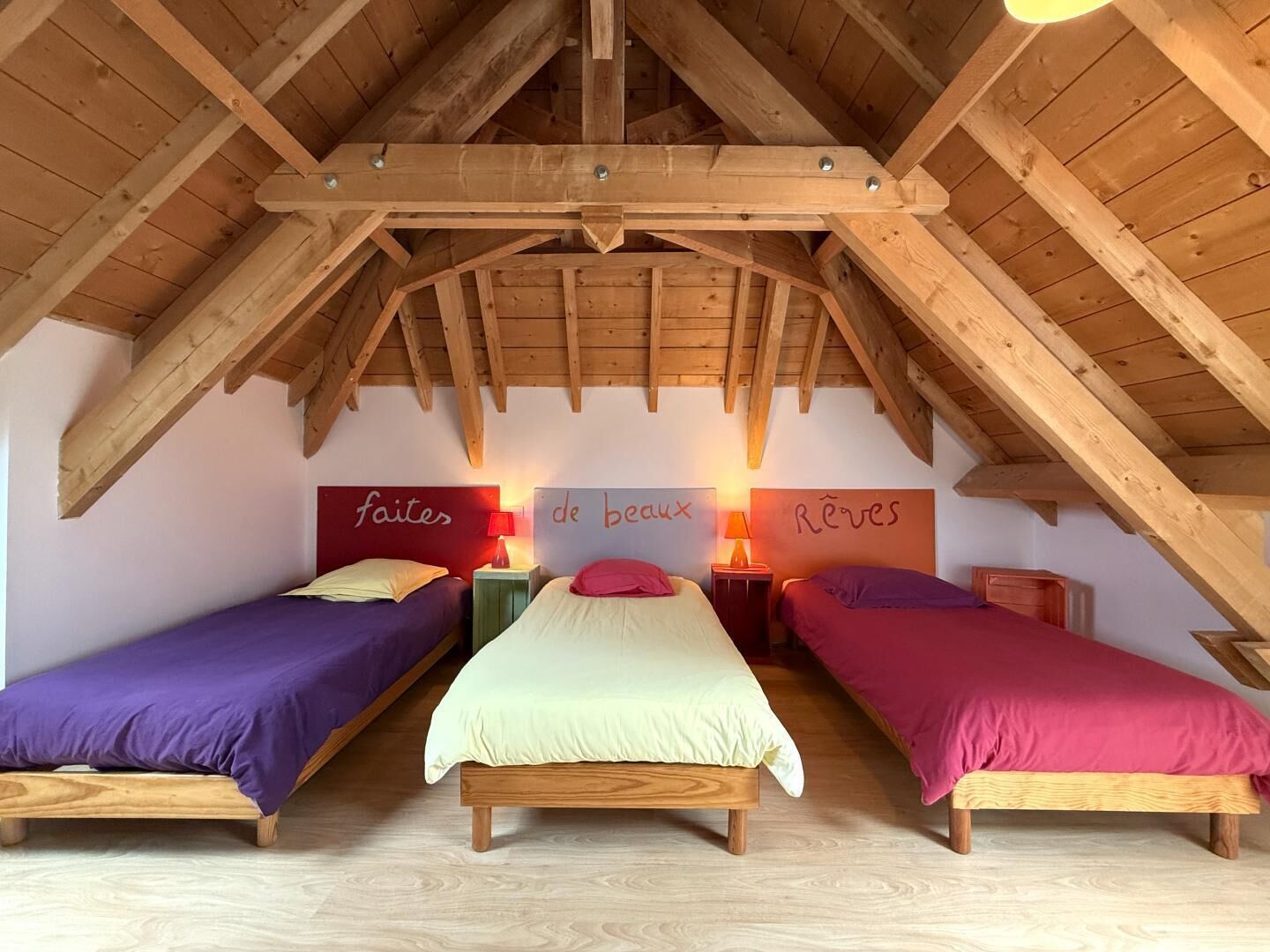Une chambre située sous les toits, avec des poutres en bois, deux lits simples, des lampes de chevet et des mots français écrits sur les murs.
