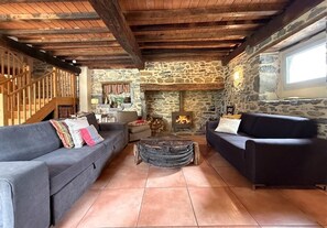 Un intérieur rustique avec des murs en pierre, des poutres en bois, une cheminée et deux canapés.