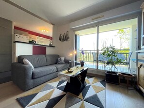 Una sala de estar moderna con un sofá gris, una mesita de centro y un tapete estampado. Hay un ventanal corredero que da a un área exterior con balcón.