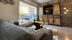 Una sala de estar con sofá, una mesa de comedor con sillas, un mueble de televisión con armarios y un balcón con mesa y sillas.