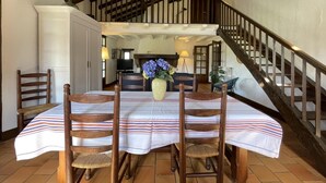 A dining area with a table set for four, wooden chairs, a vase with flowers, and a staircase leading to an upper level.