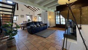 A spacious living room with a blue sofa, a dining area with a table and chairs, and a large window providing natural light.