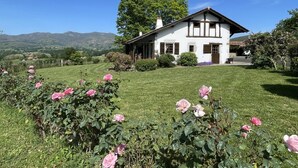 A white house with a gabled roof, surrounded by a well-maintained lawn and blooming pink roses.